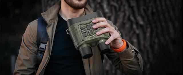 Hunter carrying compact green night vision binoculars with neck strap outdoors
