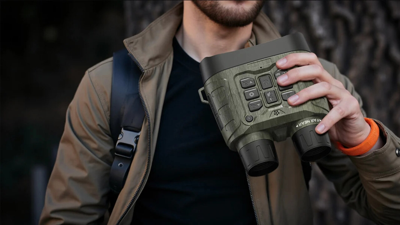 An outdoor observer holding digital night vision binoculars beside trees