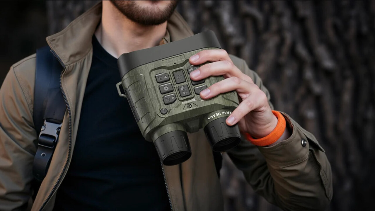 An outdoor observer holding digital night vision binoculars beside trees